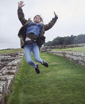 Girl leaping into the air with raised arms near stone wall