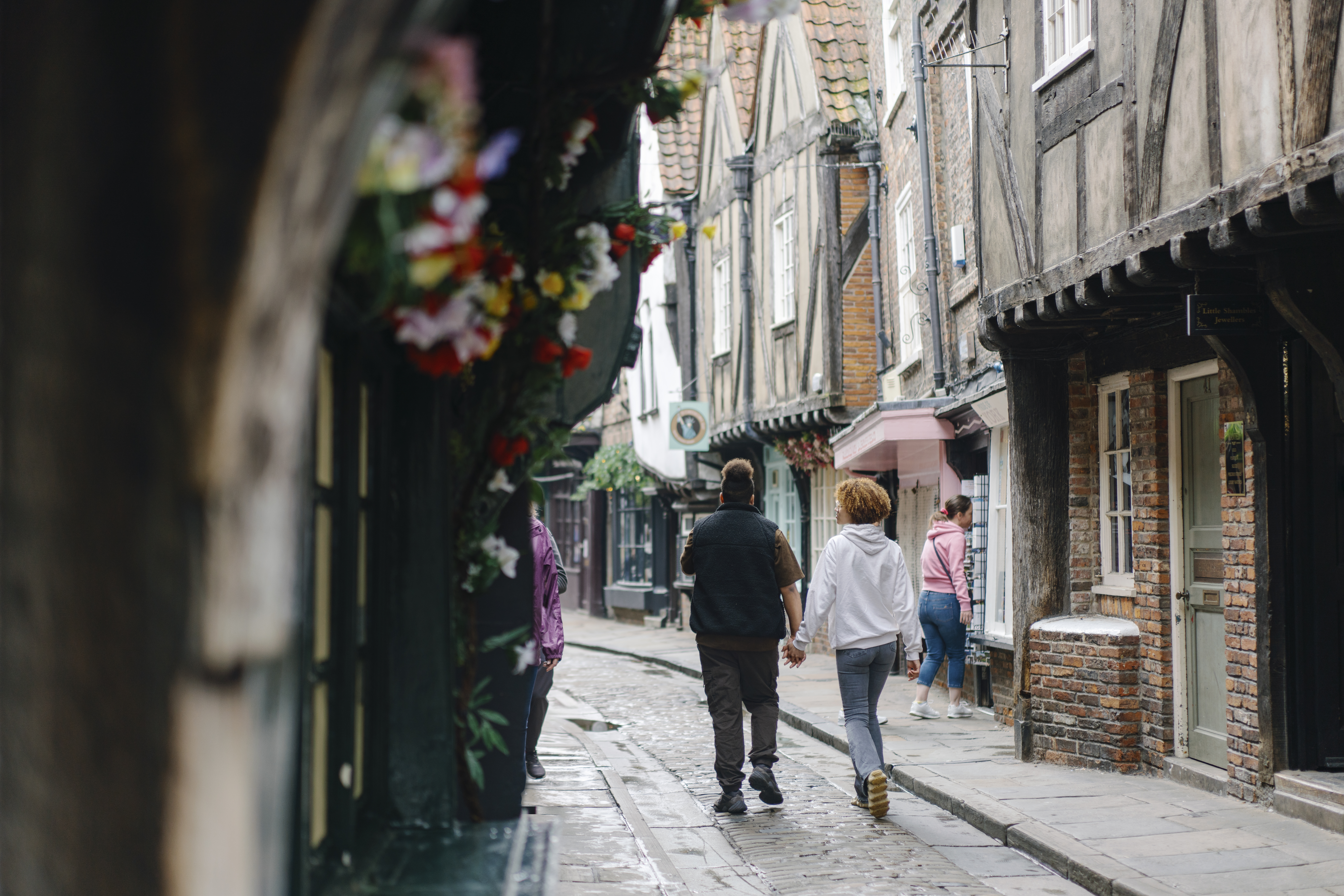 A man and a woman walk down a cobbled street holding hands