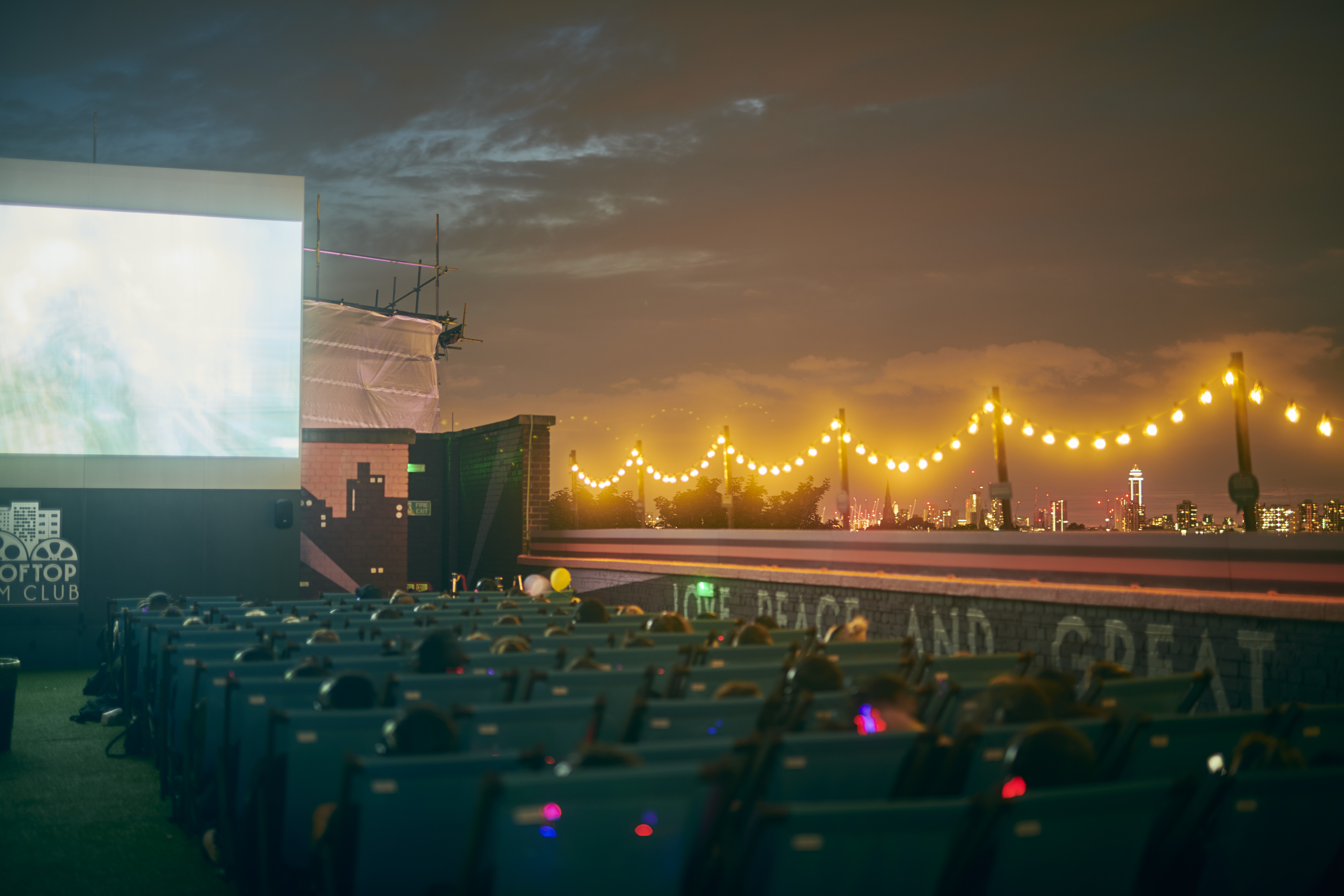 People watching a movie on a large screen at night with the city skyline in the distance