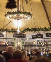 Menschen vor einer Bar in einem Festzelt, beleuchtet mit Lichterketten