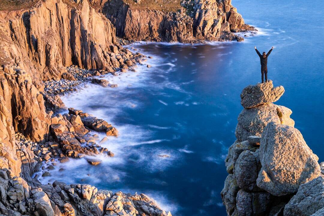 Man standing on a rocky peak on the edge of the coast looking over the headland