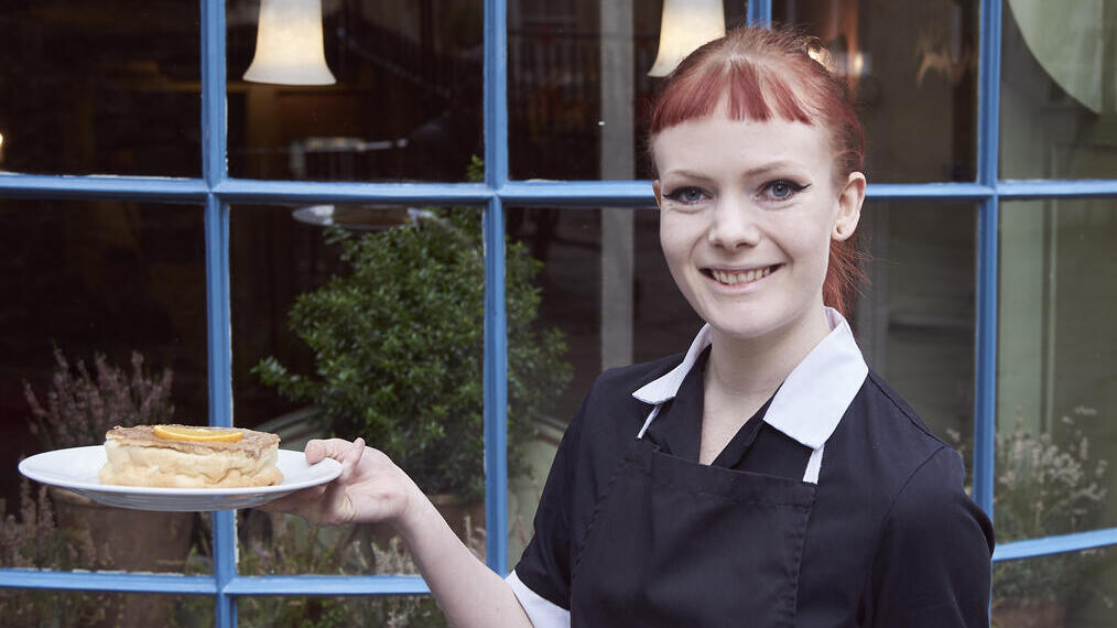 Member of restaurant staff holding a tray with tea and a cake on a plate