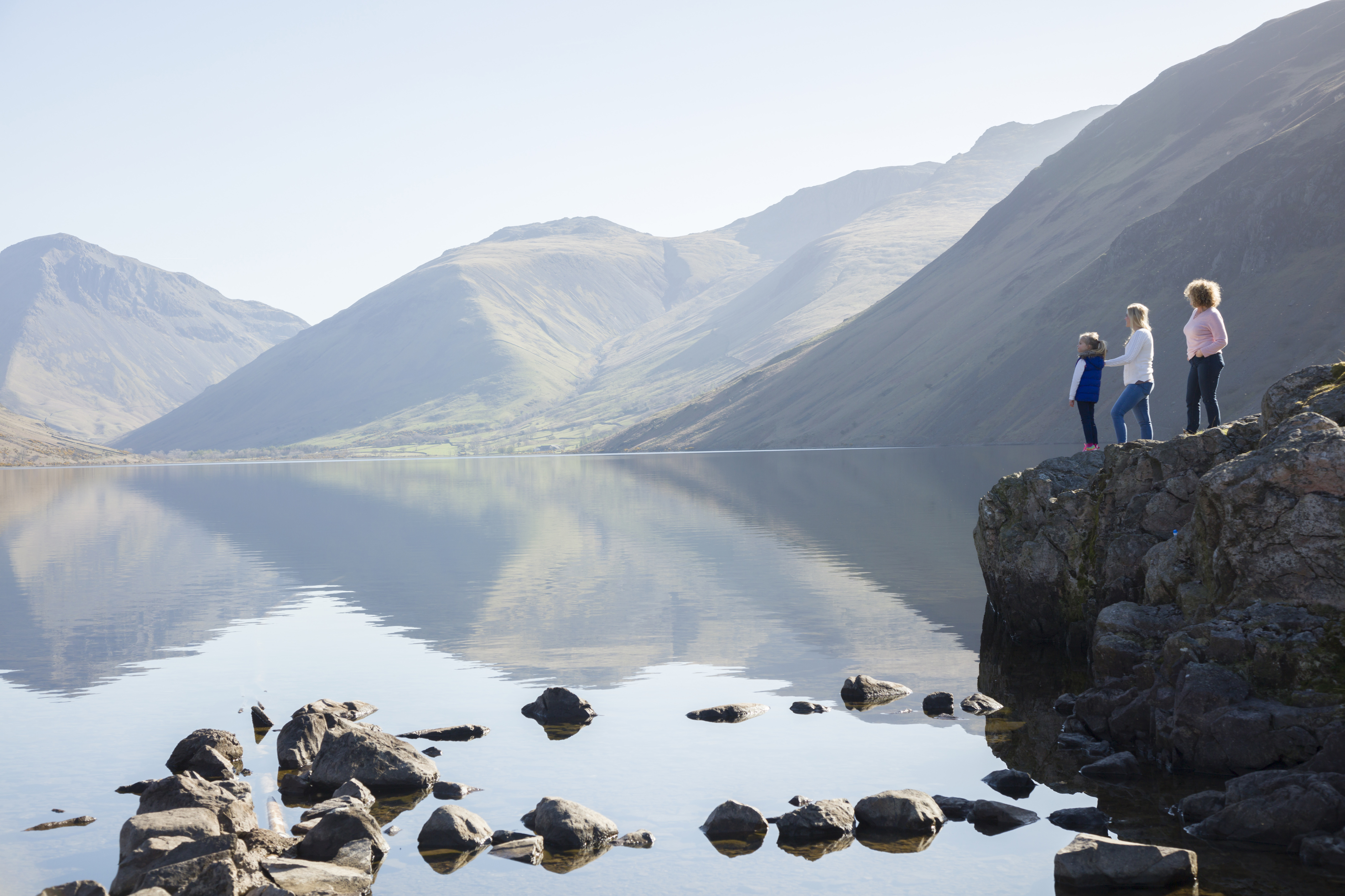 Two women and child standing on a rock overlooking lake