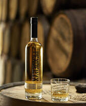 A bottle of whisky and a glass of whisky standing on an oak barrel