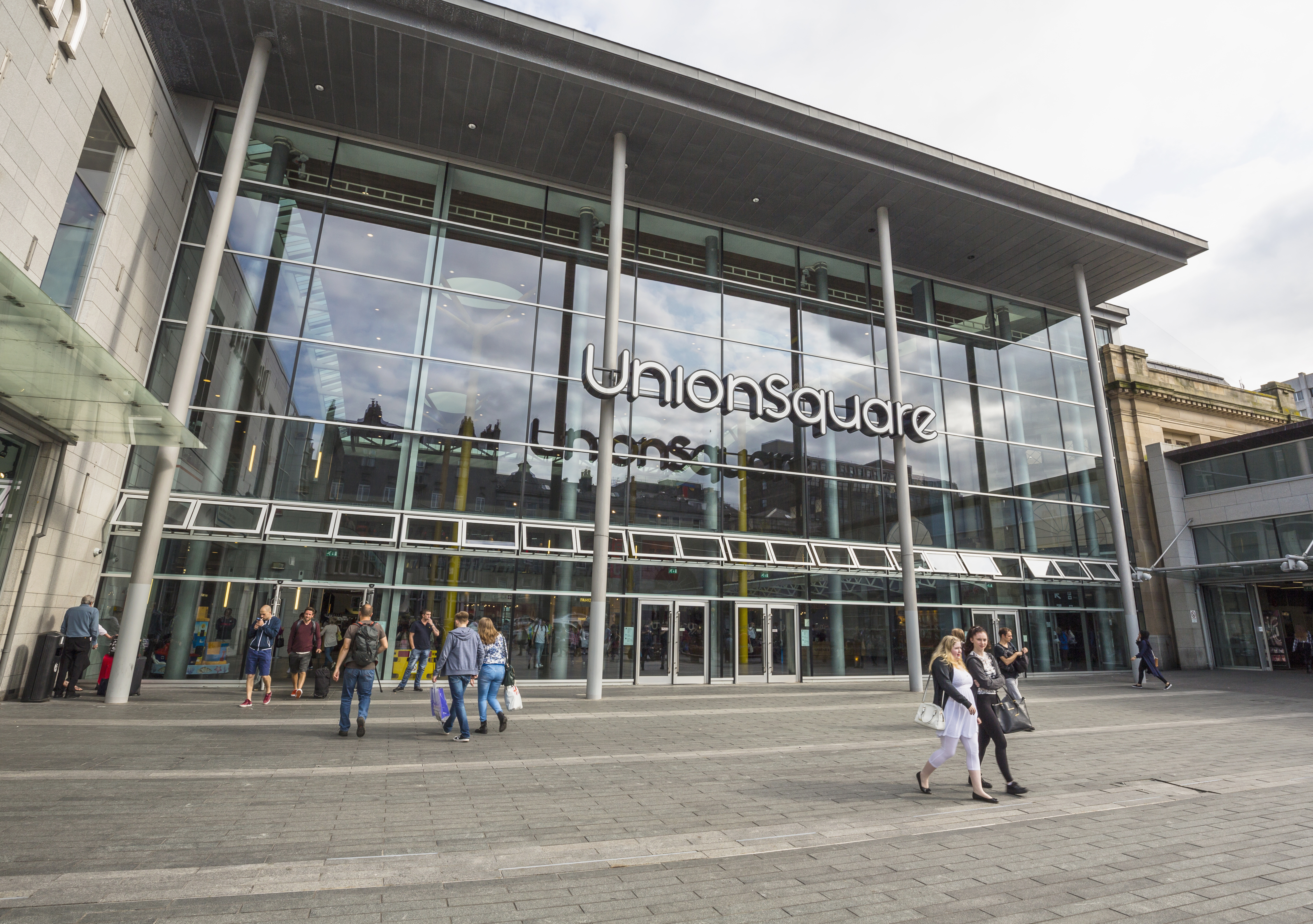 People carrying bags of shopping walking around outside of a modern shopping centre.
