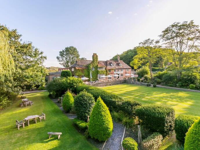Aerial shot of a country house hotel, surrounded by manicured lawns with picnic tables.