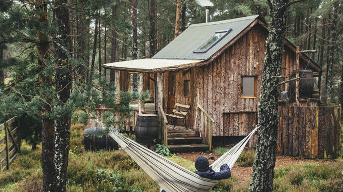 Man relaxing in a hammock outside a wooden cabin in a forest