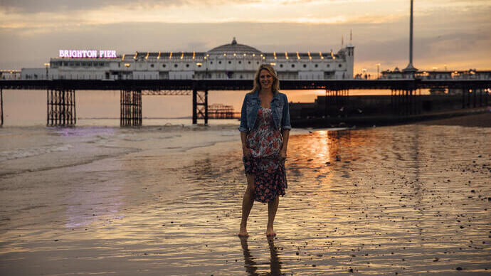 Woman standing on the beach near the pier at sunset