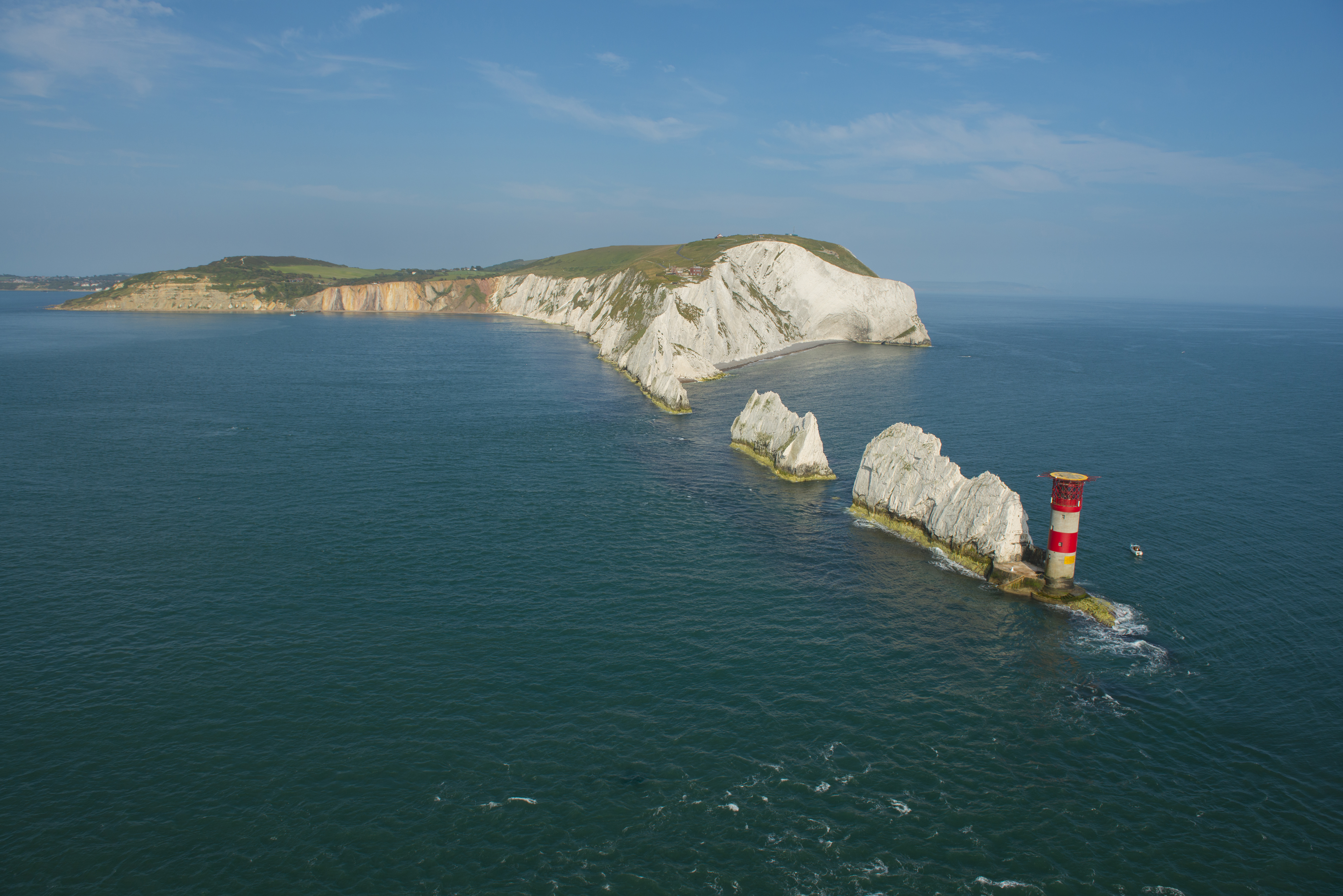 Tall chalk stacks in a row running from the cliffs of the mainland to a lighthouse