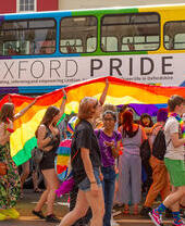Multitud de personas frente a un autobús con los colores del arcoíris como parte del Orgullo de Oxford