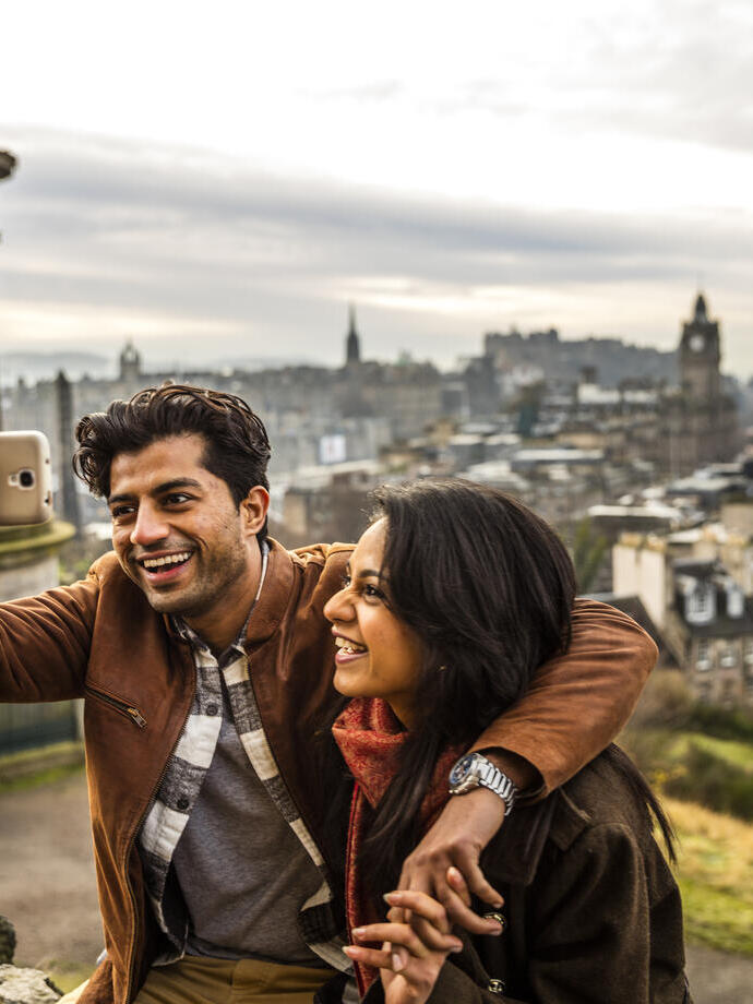 Couple prenant un selfie avec un téléphone portable, avec une ville en arrière-plan