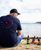 Un uomo seduto sulla spiaggia accanto a bottiglie di birra artigianale Snowdon