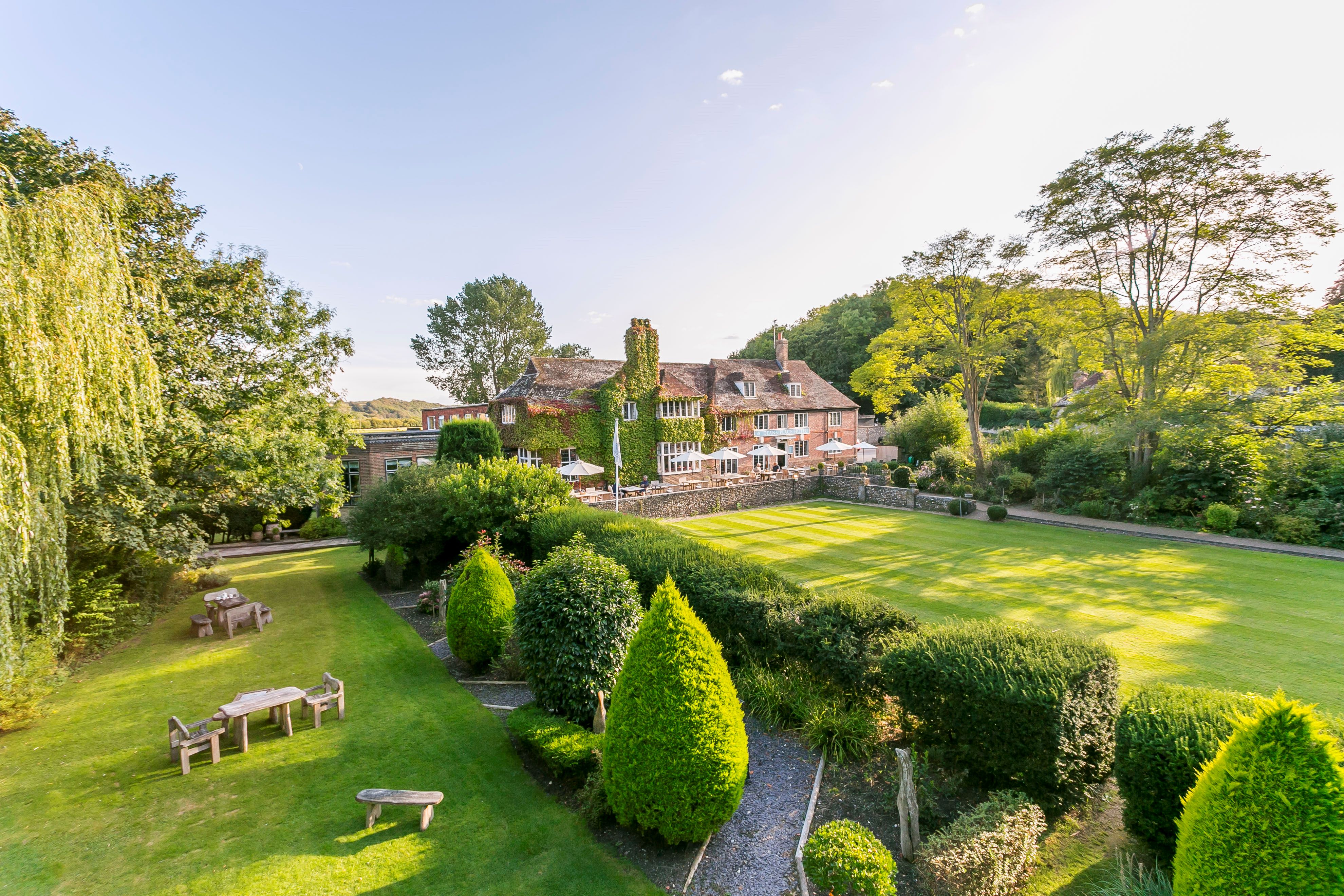 Aerial shot of a country house hotel, surrounded by manicured lawns with picnic tables.