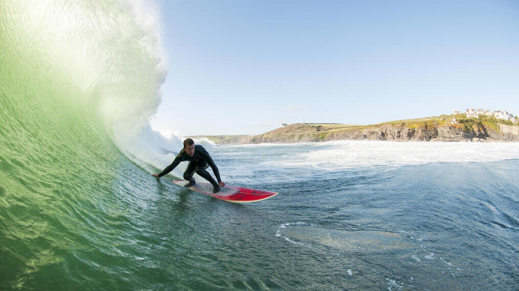 راكب أمواج يرتدي بذلة غطس يركب موجة كبيرة على لوح تزلج أحمر في البحر