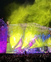 A crowd of people in front of the stage of a musical festival at night.