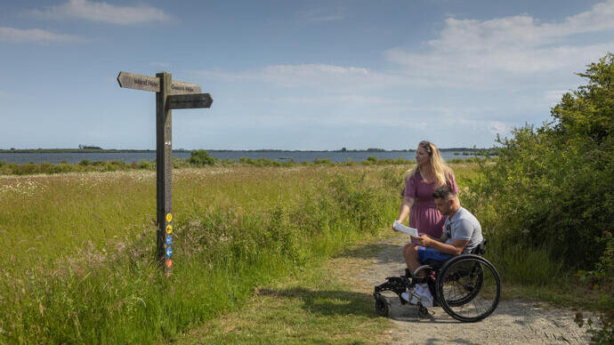 A man who uses a wheelchair and a woman review a map in the countryside