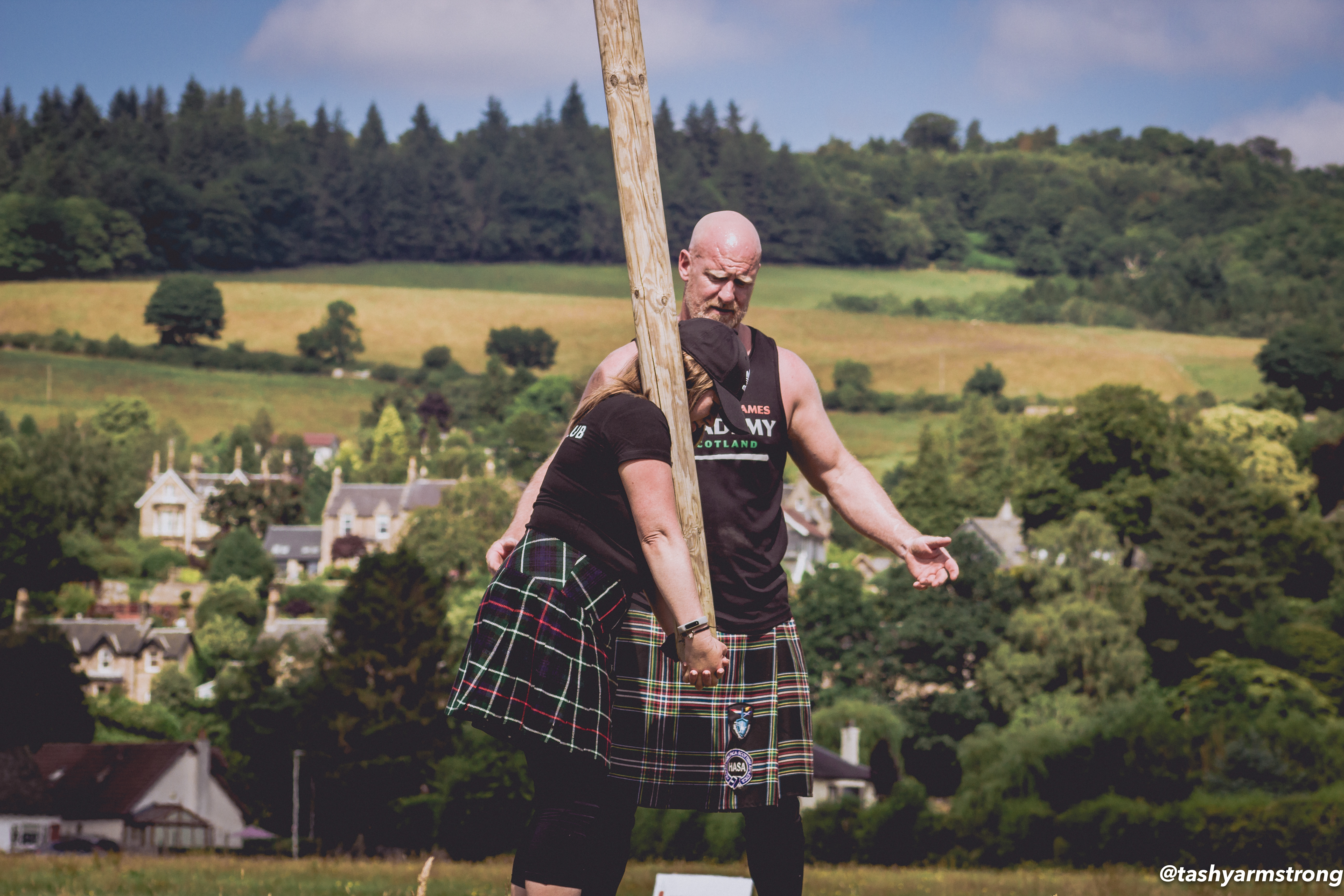 Woman wearing a kilt learning how to toss the caber with male instructor
