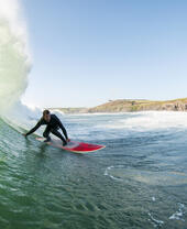 Surfer in a wetsuit surfing a large wave on a red surfboard in the sea