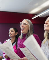 Un grupo de mujeres en un coro con partituras cantando en un estudio de grabación musical.