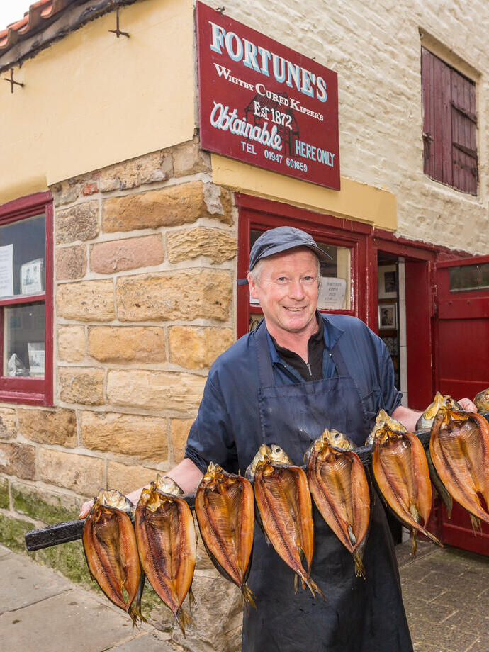Chief Kipper Smoker standing outside Fortune's Kippers holding a row of smoked kippers