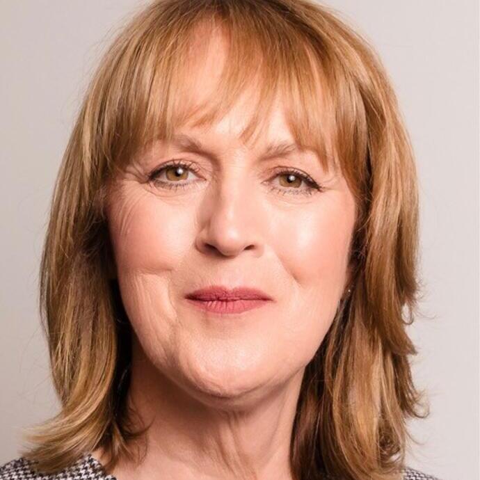 Portrait of a middle-aged woman with shoulder-length light brown hair, wearing a black and white patterned top, smiling slightly, with a plain background.