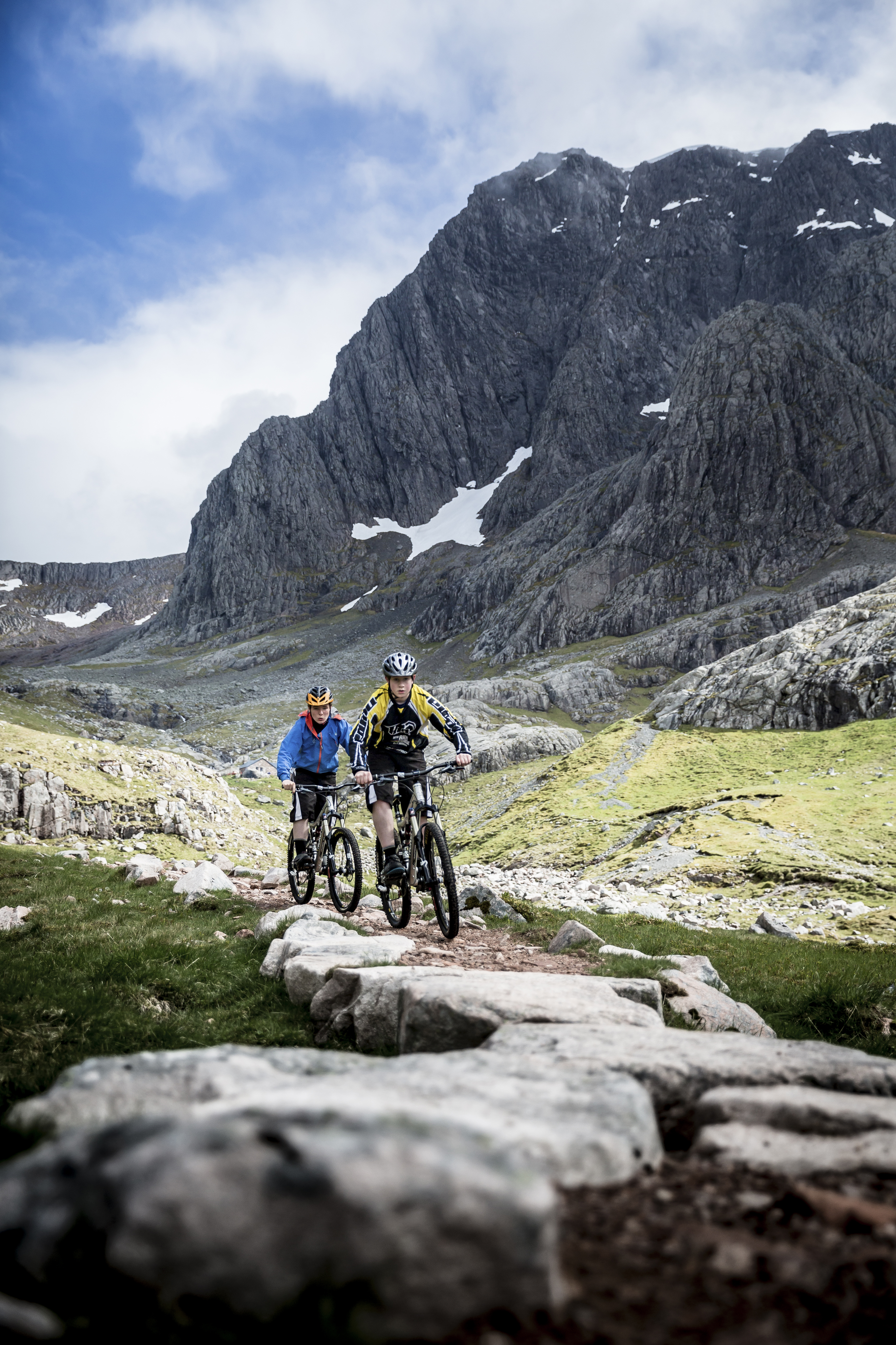 Two mountain bikers cycling up a mountain on a narrow rocky path