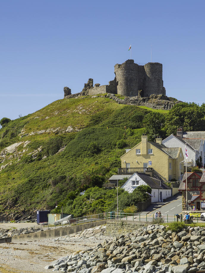 Un château au sommet d'une colline à côté d'une plage, entouré de bâtiments colorés.