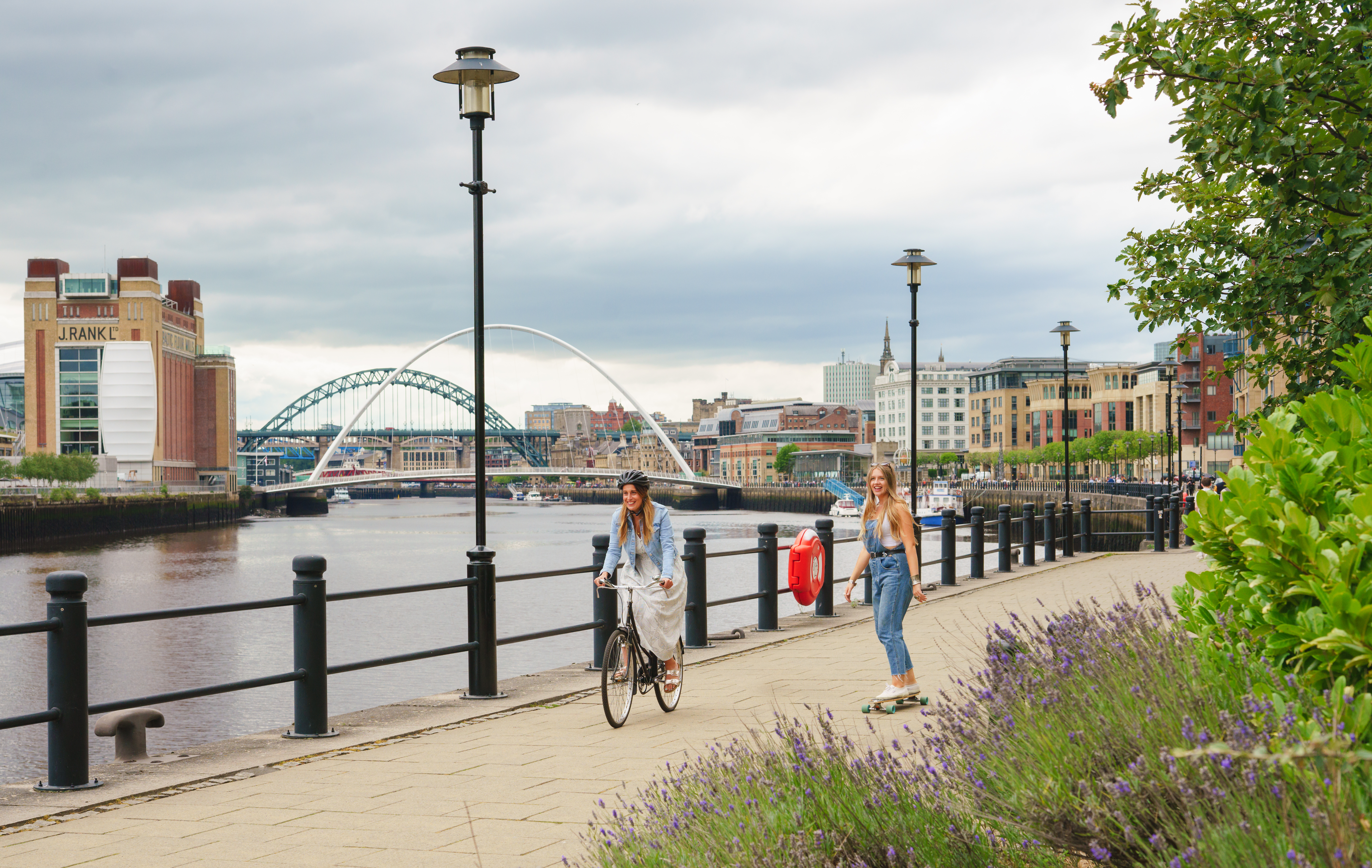 Two people cycling and skateboarding on a path along the River Tyne in Newcastle.