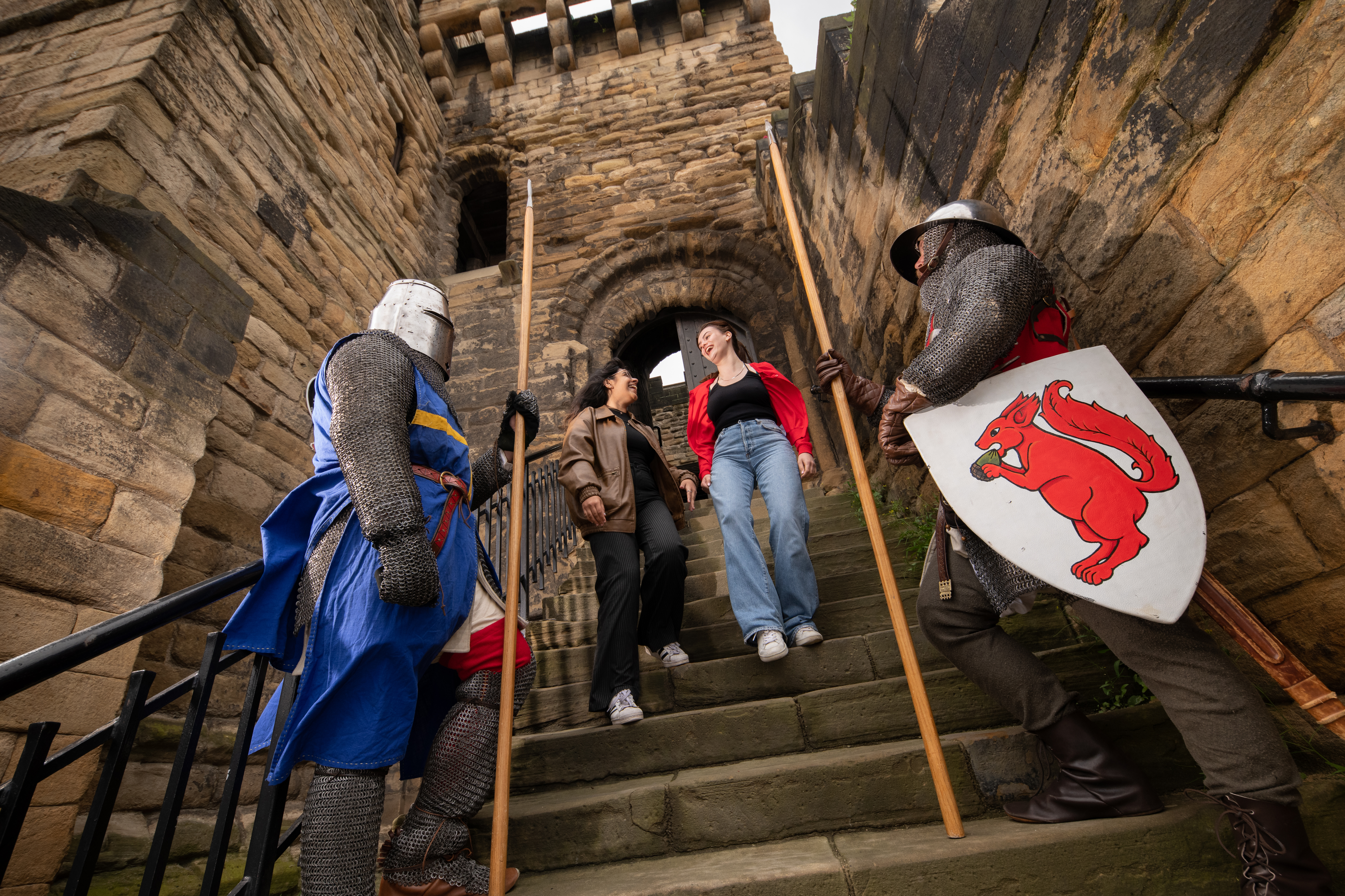 Two women explore a castle while two men stand in medieval costume