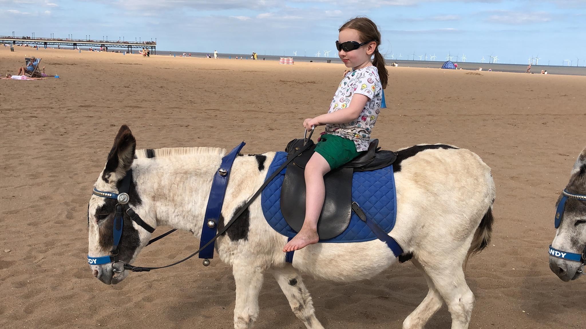 Ein Kind reitet auf einem Esel am Strand von Skegness